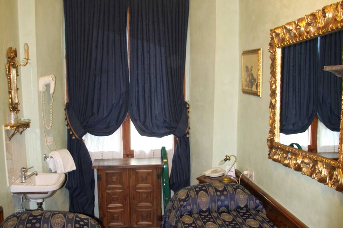 A room with two beds, a wooden dresser, a mirror, a sink, and a window with curtains.