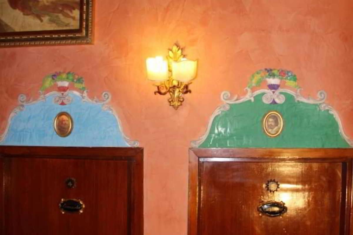 Dos puertas de madera con diseños ornamentales y una lámpara fijada a la pared en el centro.