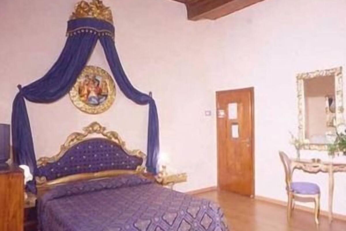 A bedroom with a four-poster bed, a ceiling fan, a wooden floor, and a mirror on the wall.
