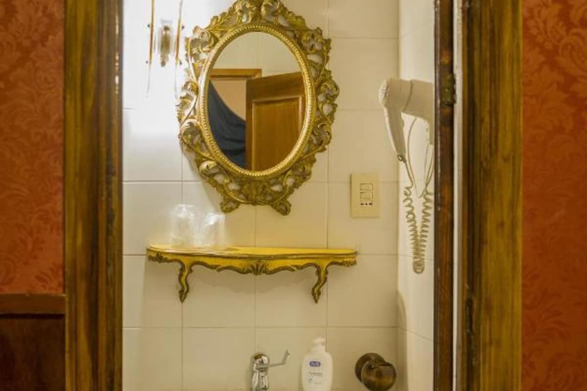 A bathroom with a white sink, a gold-framed mirror, a hairdryer, and a towel rack.