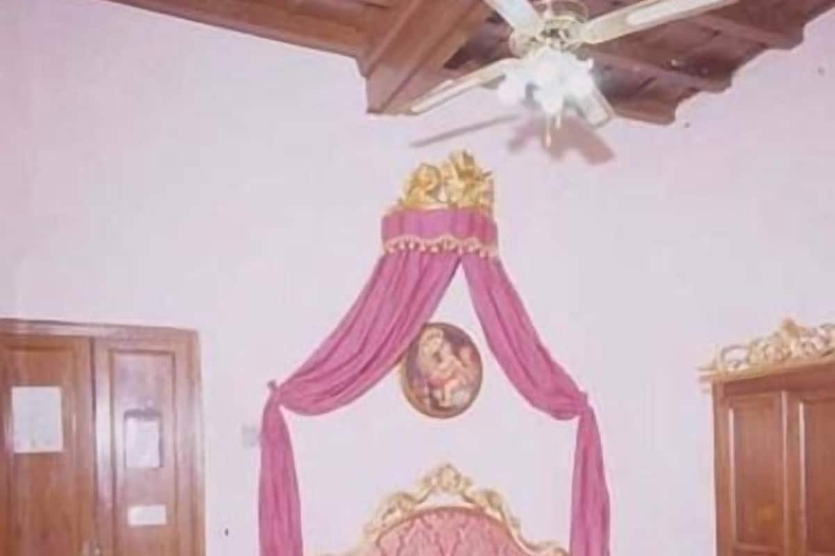 A bedroom with a four-poster bed, wooden wardrobe, and a ceiling fan.