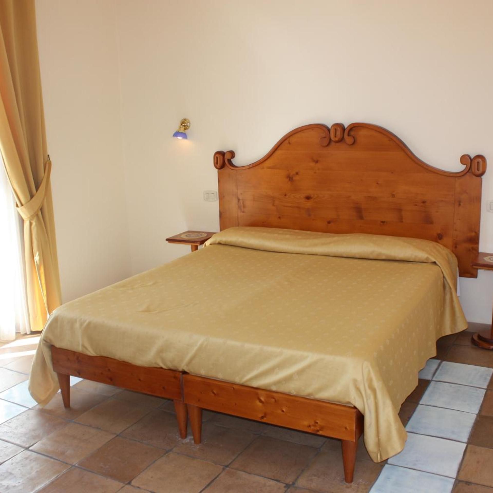 A single bed with a wooden headboard, a bedside table, and a lamp on the wall.