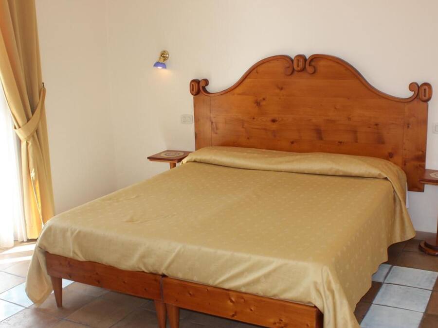 A single bed with a wooden headboard, a bedside table, and a lamp on the wall.