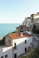 Un edificio costiero con facciata in pietra, tetto in tegole rosse e vista sul mare.