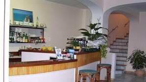 A bar area with a wooden counter, bar stools, and various bottles. There is a staircase in the background leading to an upper level. - Belvedere Sperlonga (Sperlonga)