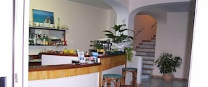 A bar area with a wooden counter, bar stools, and various bottles. There is a staircase in the background leading to an upper level. - Belvedere Sperlonga (Sperlonga)