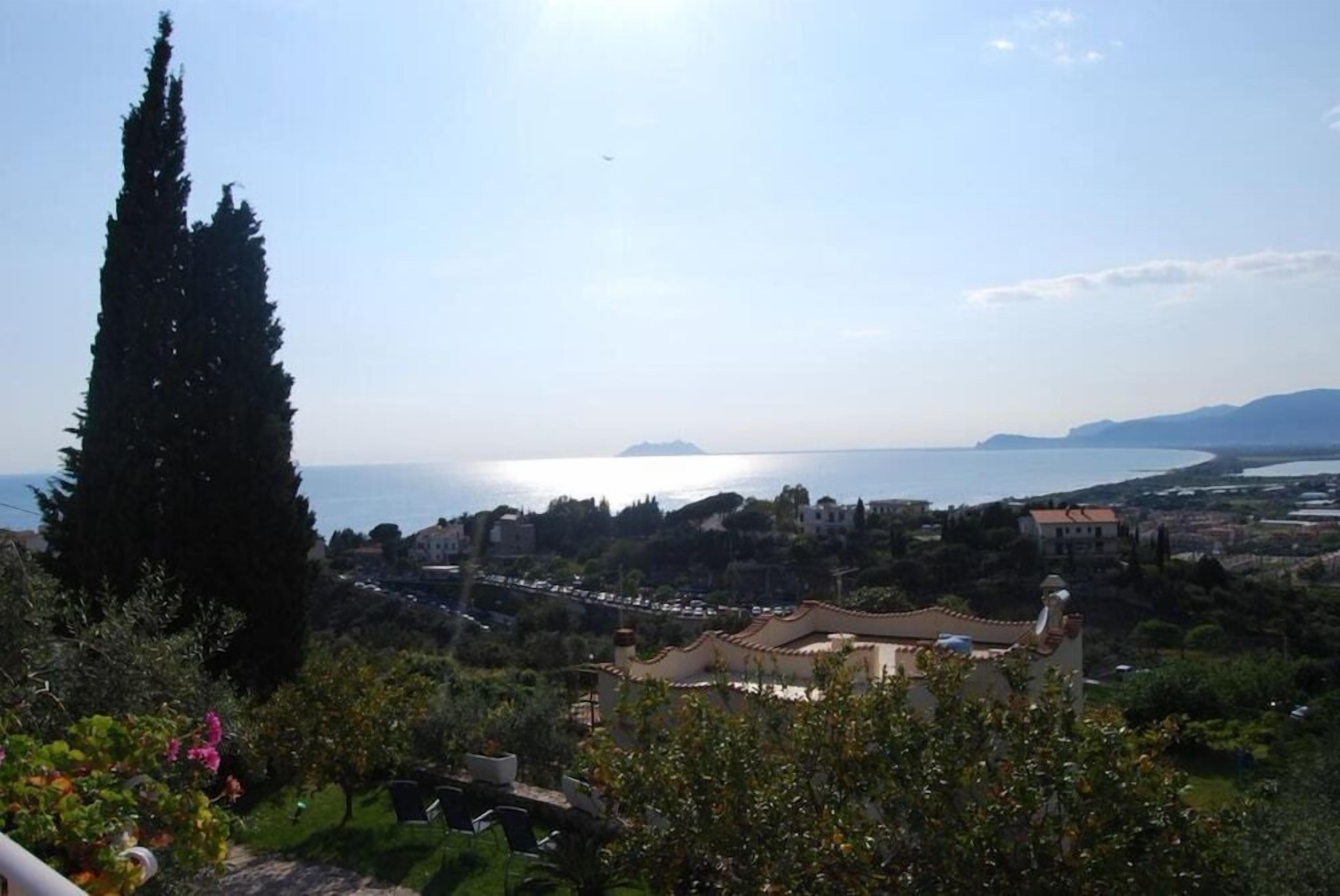 Un borgo costiero con vista sul mare, edifici dall'architettura mediterranea e un cipresso ben visibile.