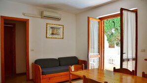 Una habitació amb taula i cadires de fusta, un sofà i un gran finestral amb cortines.