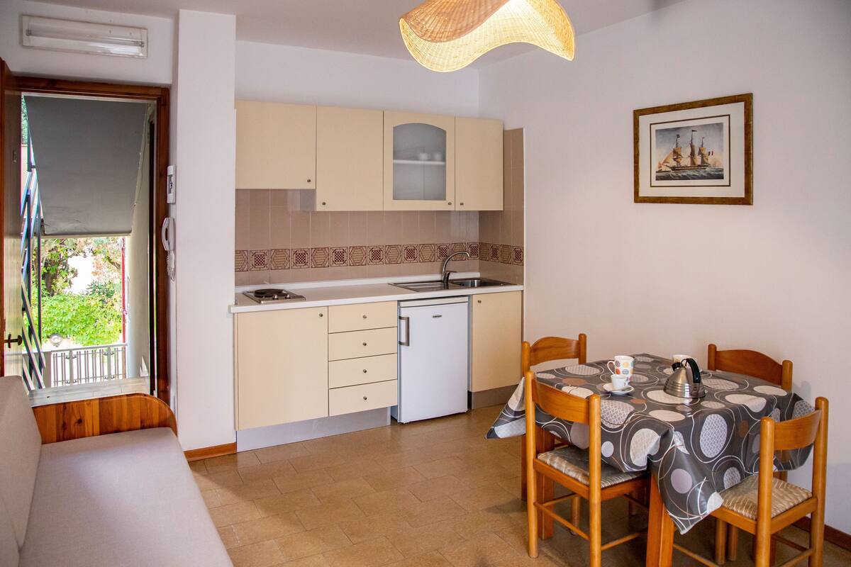 A compact kitchen with a dining area, featuring a small refrigerator, a sink, and a dining table set with chairs.