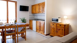 Cuina amb armaris de fusta, microones i zona de dinar amb caires i taula.