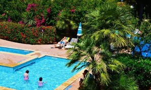 A swimming pool surrounded by lush greenery and palm trees. - Residenza Gli Eucalipti (Alghero)