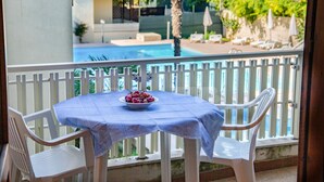 Un balcó amb una taula preparada per a dues persones, un bol de fruita i una piscina al fons.
