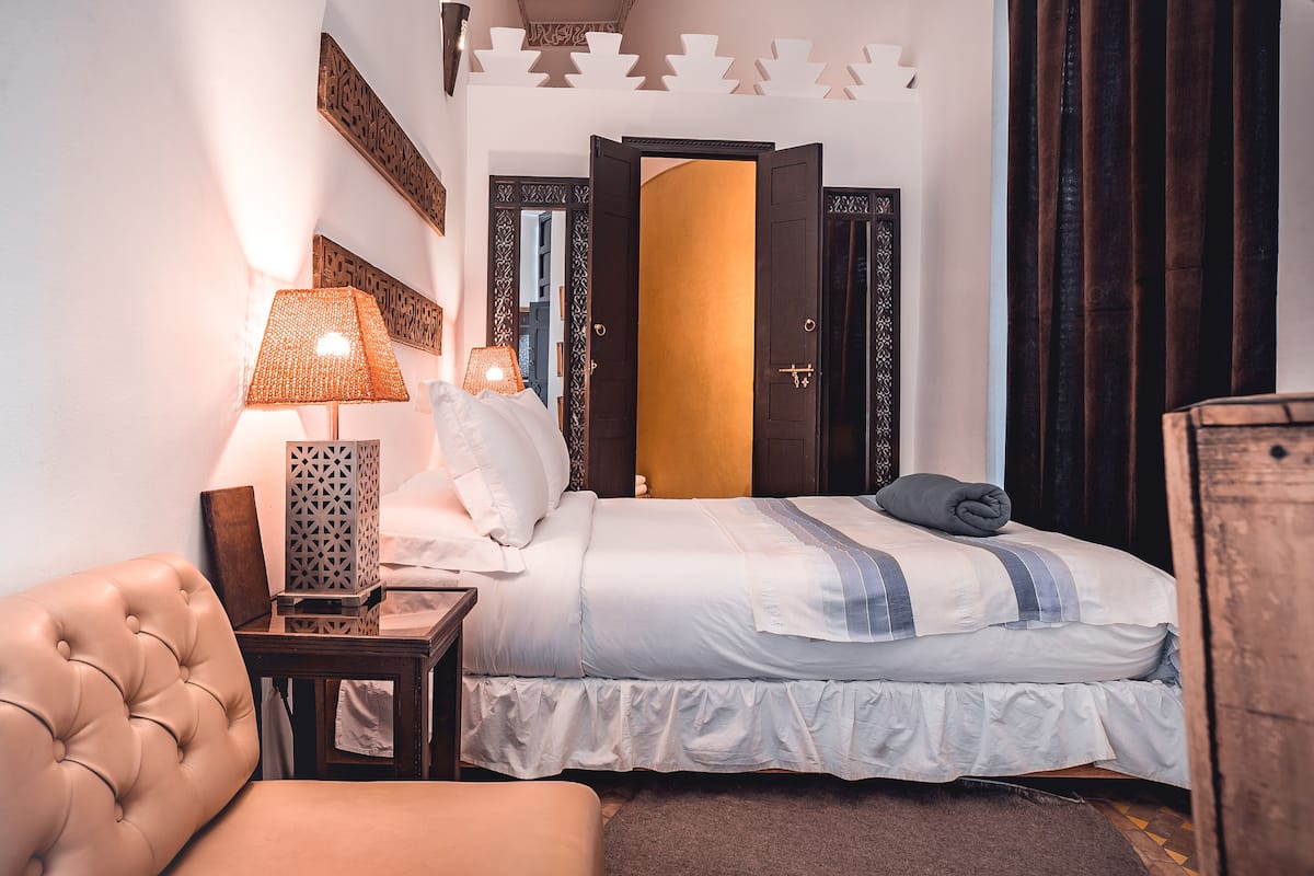 Et hotelværelse med en seng, en lampe, en stol og en træsenggavl.