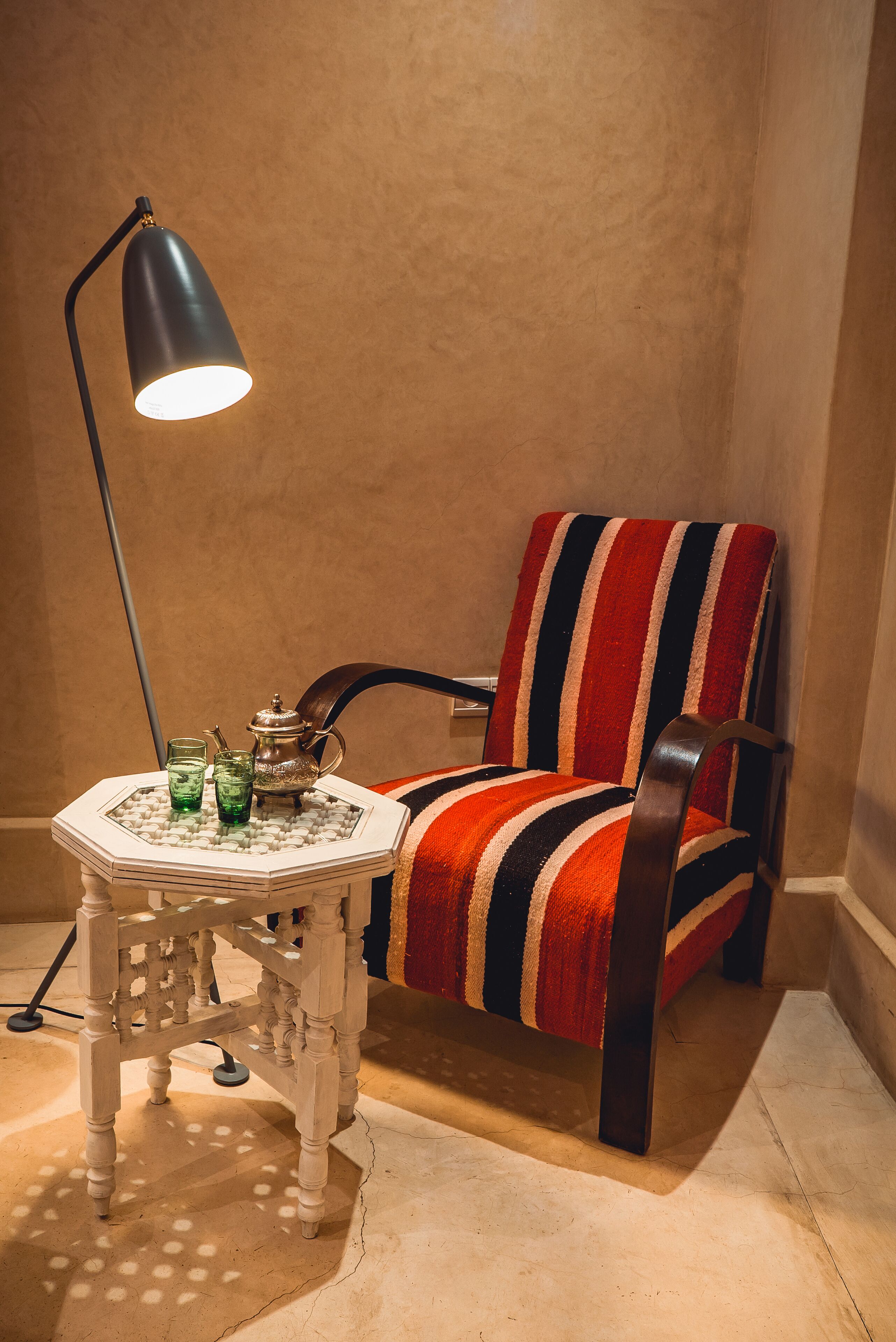 A corner of a room with a striped armchair, a small round table with a lamp, and a decorative tray.