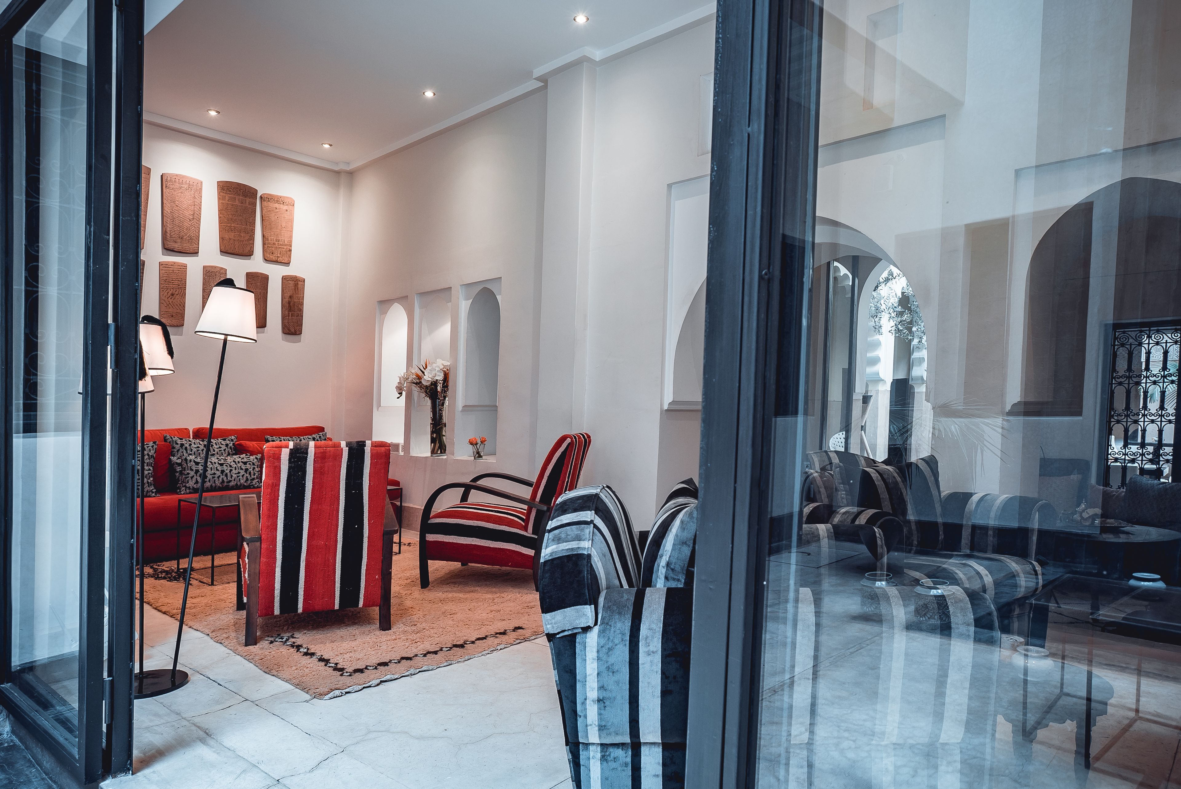 A modern living room with a red sofa, striped armchairs, and a glass coffee table.