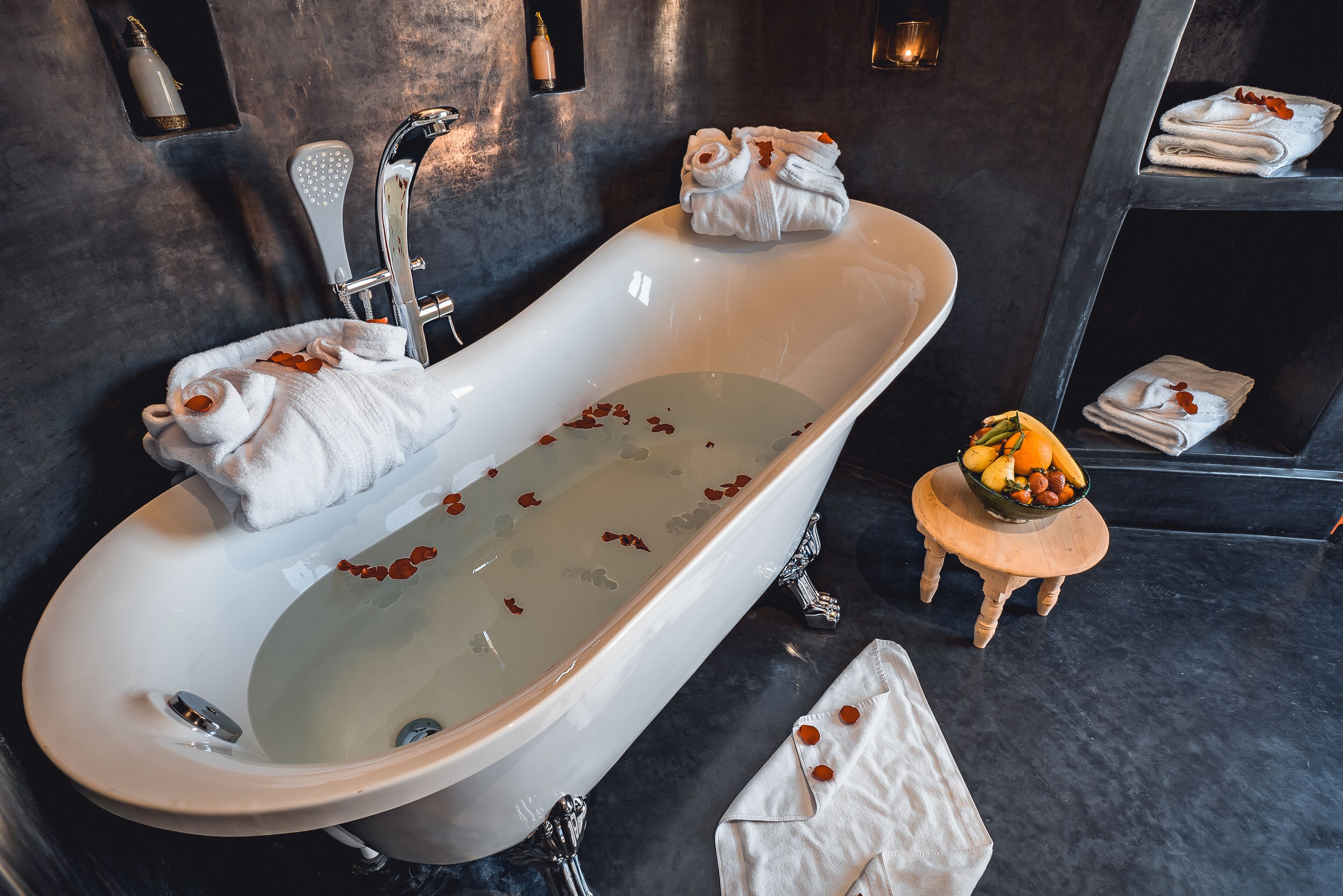 Un baño moderno con una bañera independiente, un taburete de madera con frutas y toallas ordenadas en estantes.