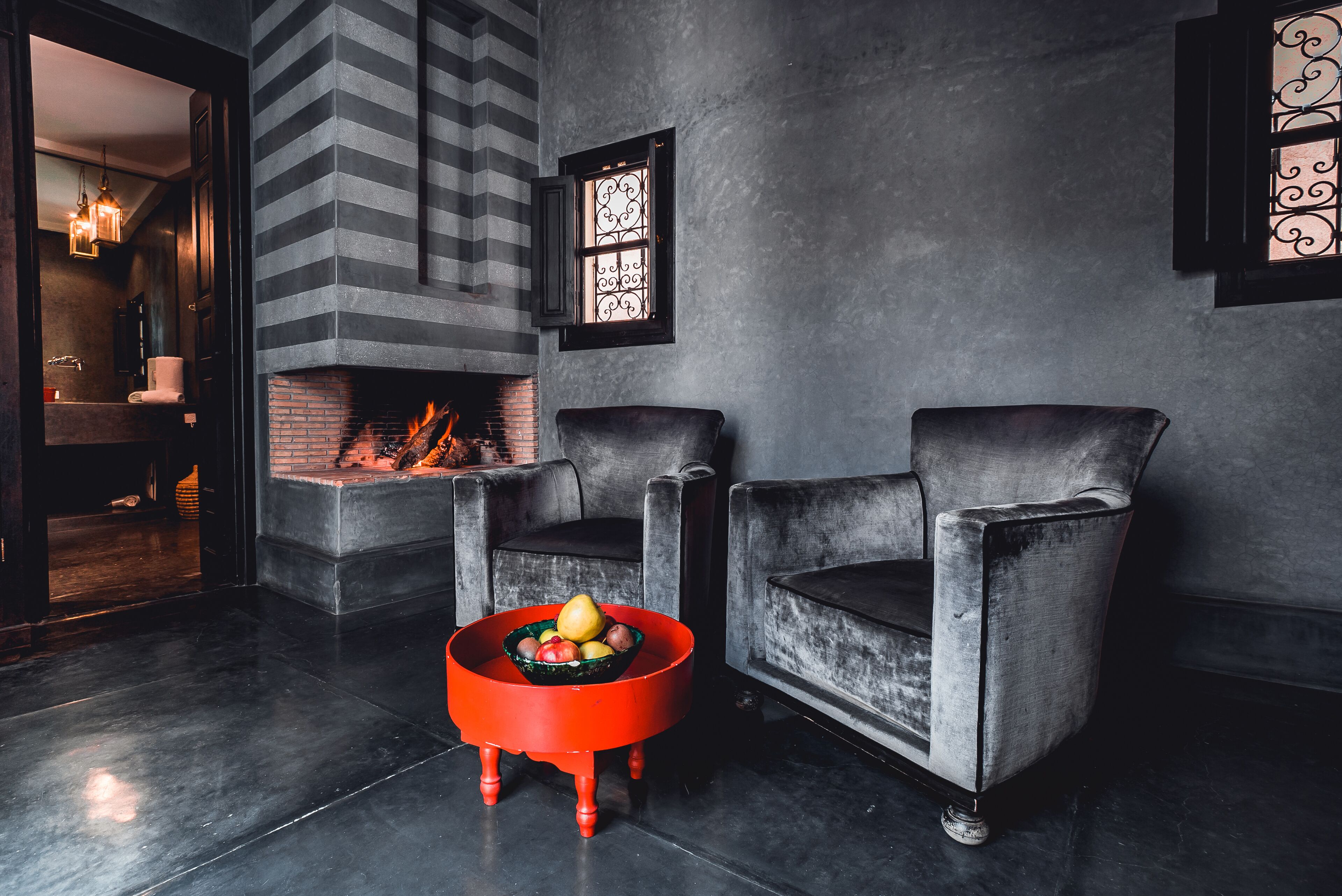 A modern living room with a fireplace, two armchairs, and a red side table with fruit.