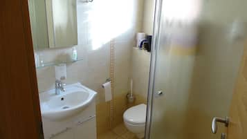 Een badkamer met een witte wastafel, spiegel en toilet. Er is een glazen douchedeur en een handdoekhouder.