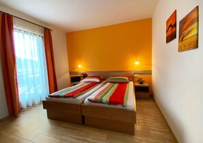 Une chambre d’hôtel avec deux lits, une grande fenêtre avec des rideaux, deux lampes fixées au mur et des œuvres d’art accrochées au mur.