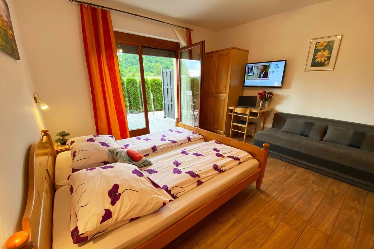 Een slaapkamer met een bed, een bank, een televisie en uitzicht op groen.
