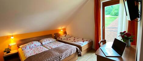 Un dormitorio con cama, escritorio con ordenador portátil, mesita de noche con lámpara y ventana con cortinas.