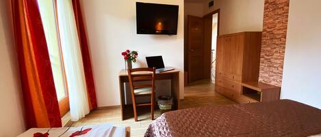 Una habitación de hotel con cama, escritorio, computadora portátil, televisor y armario.