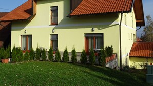 Une maison à deux étages, avec un toit recouvert de tuiles rouges, de nombreuses fenêtres et une pelouse bien entretenue agrémentée de petits arbres.