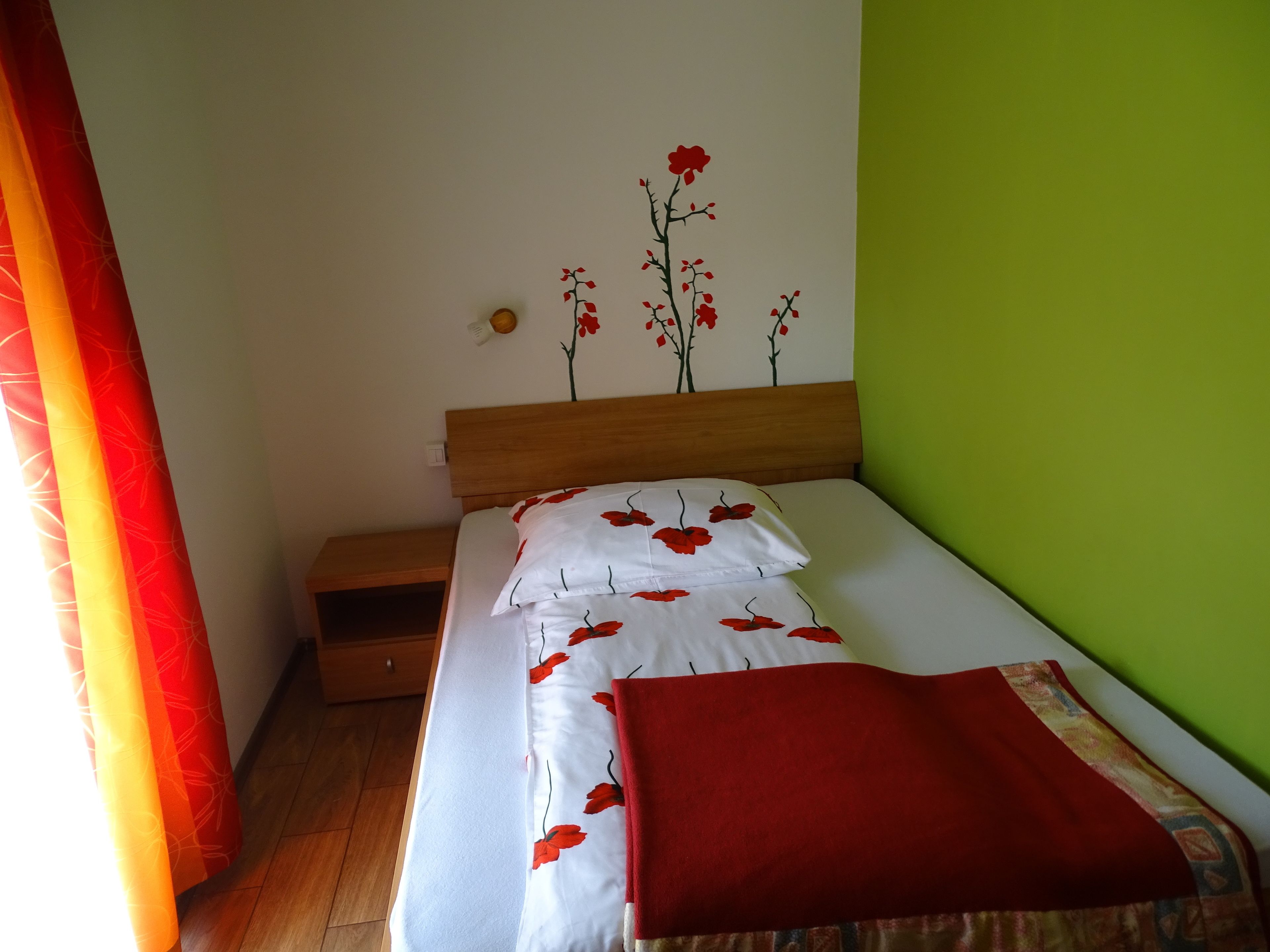 Una cama bien tendida con ropa de cama floral en blanco y rojo, un cabecero de madera y una pared verde.