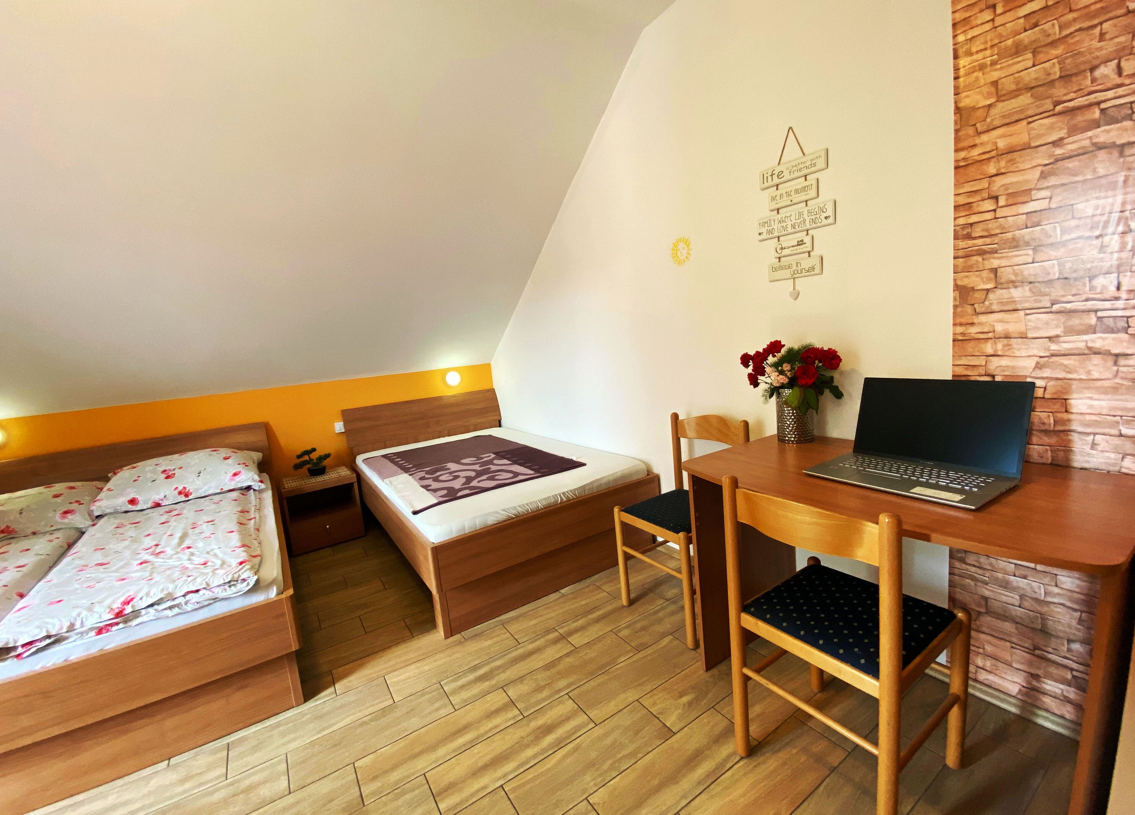 Ein Schlafzimmer mit zwei Betten, einem Schreibtisch mit einem Laptop und einem kleinen Tisch mit Blumen.