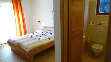 A bedroom with a wooden bed, a bathroom with a toilet, and a window with a view of the sky.