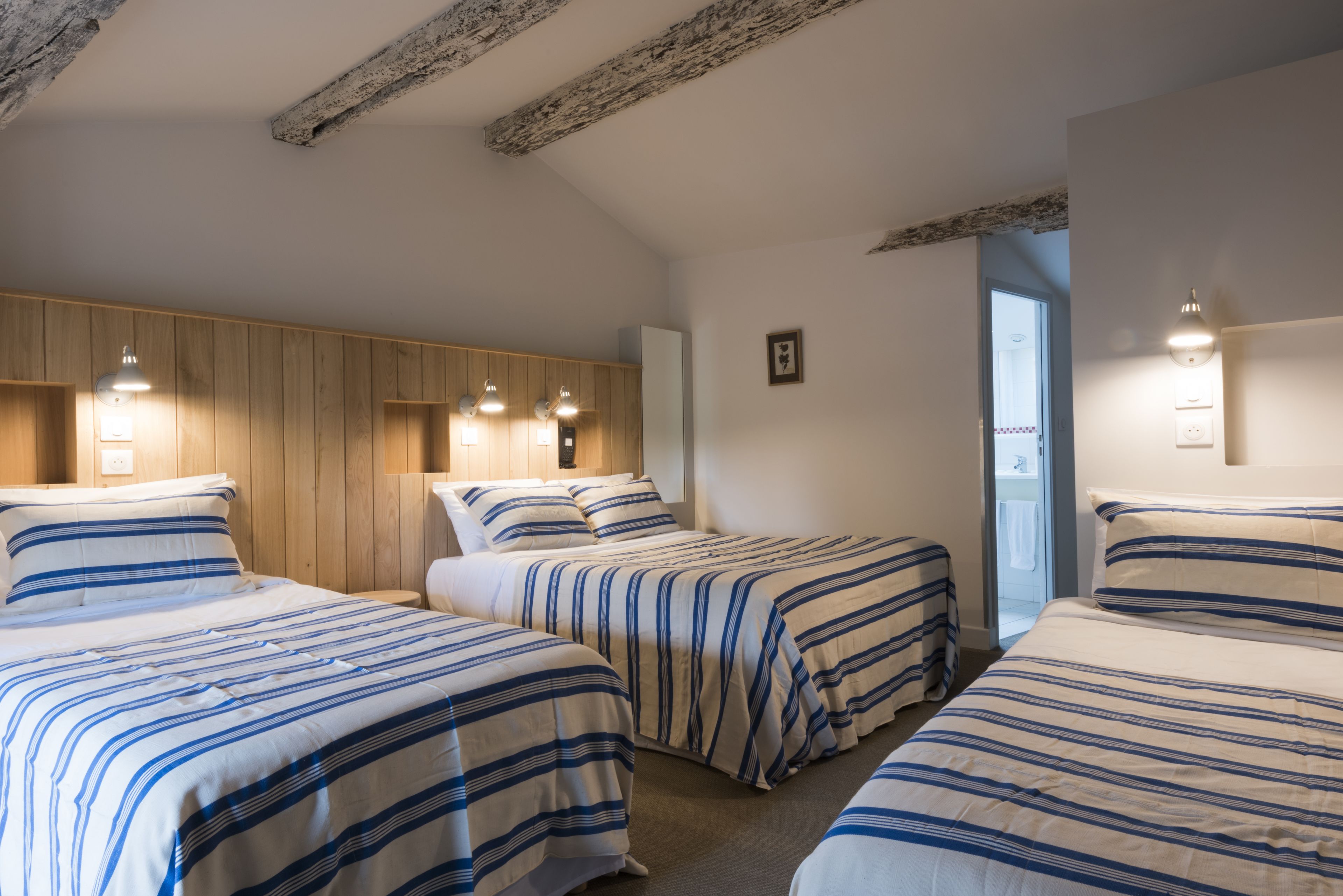 Habitación de hotel con tres camas, paneles de madera en las paredes y una puerta que da a un baño.