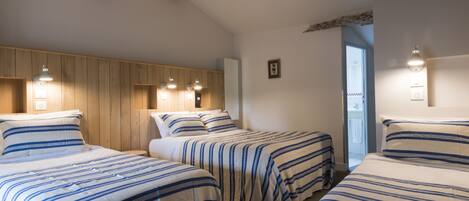 Habitación de hotel con tres camas, paneles de madera en las paredes y una puerta que da a un baño.