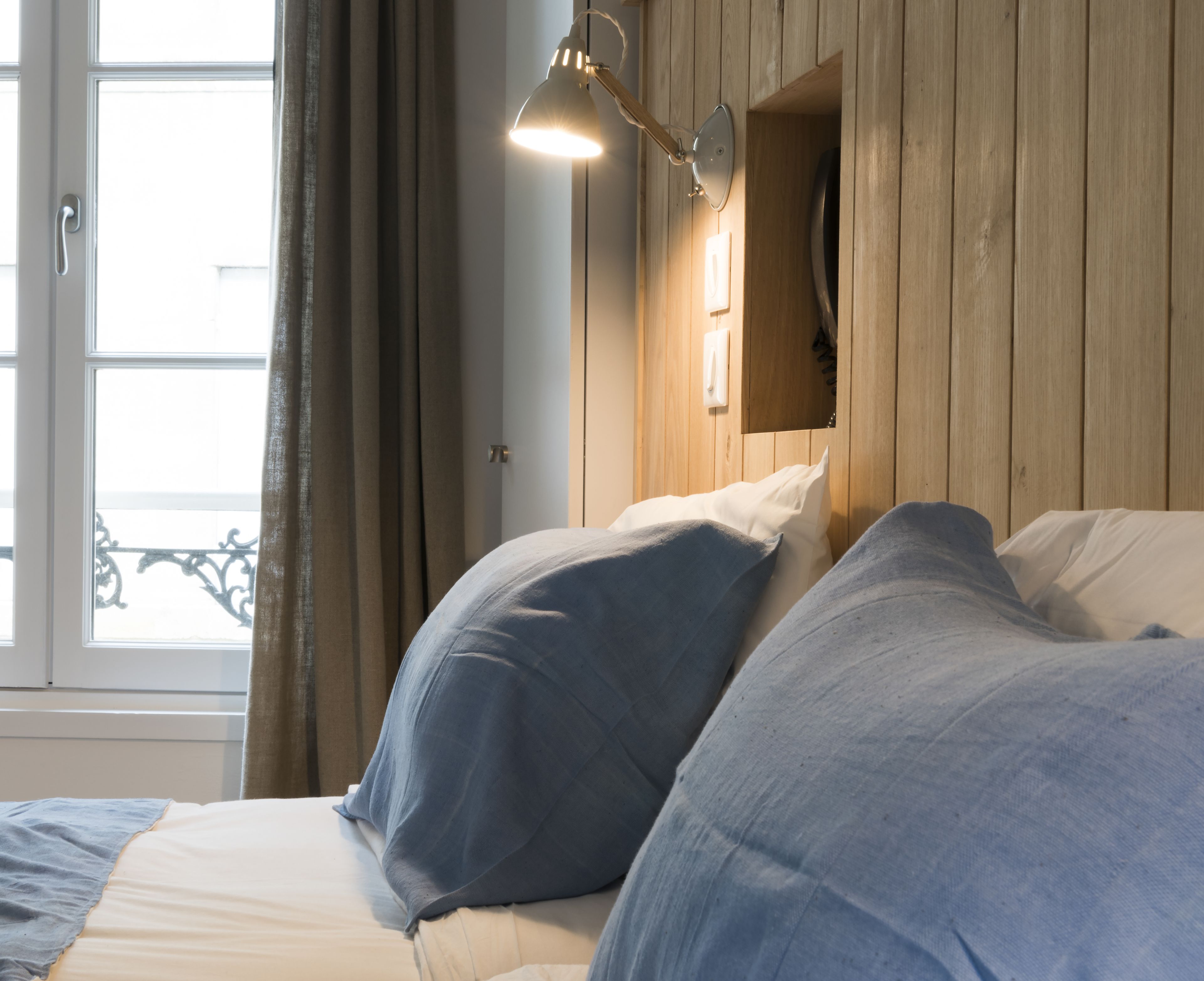 A bedroom with a wooden headboard, a bedside lamp, and a window with curtains.