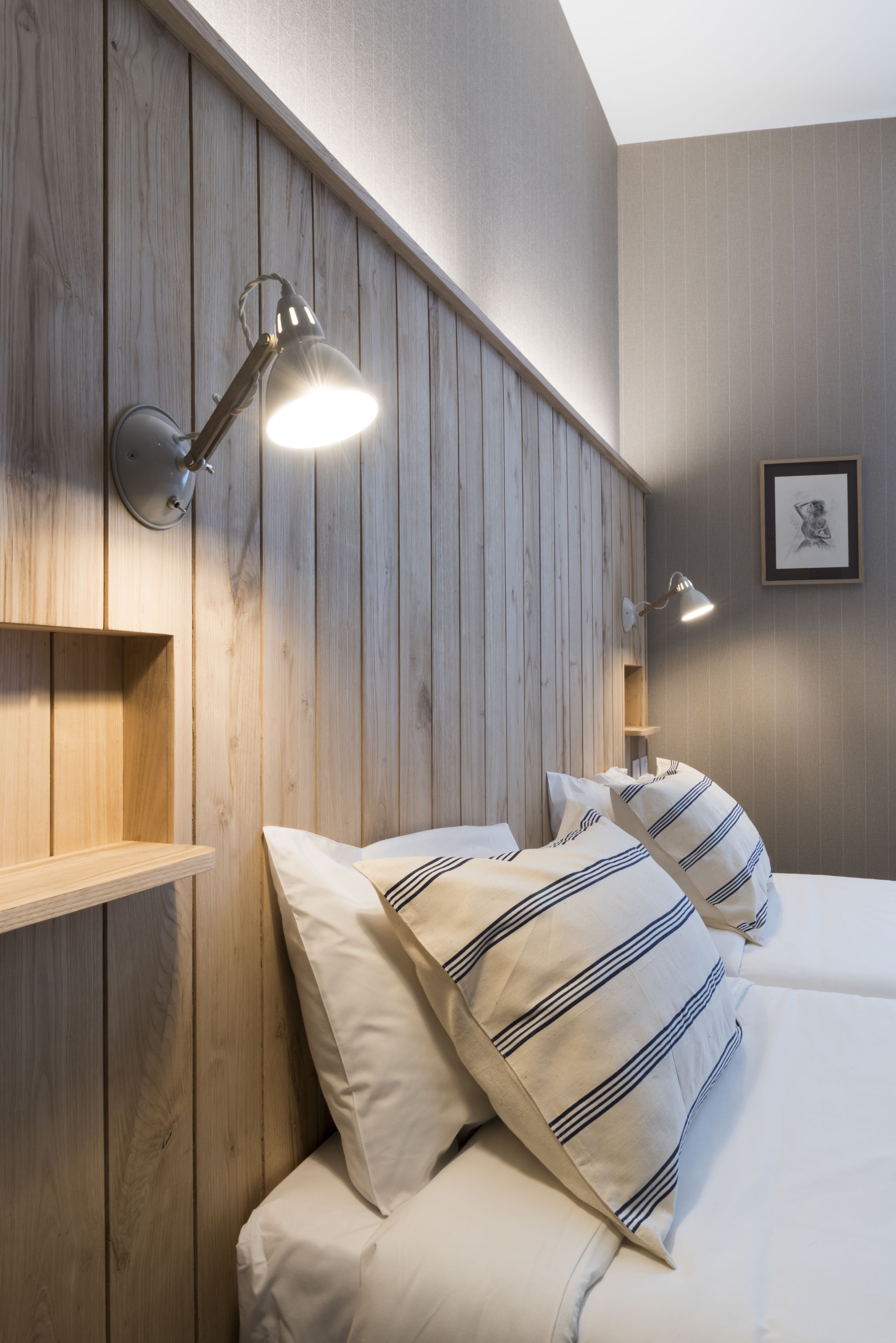 Een keurig opgemaakt slaapkamer met een houten hoofdbord, twee bedlampjes en gestreepte kussens.