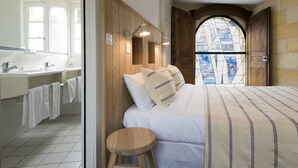 A bedroom with a large bed, wooden headboard, and a view through an arched window. - Auberge de la Commanderie (Saint-Émilion)