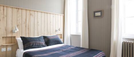 A bedroom with a wooden headboard, a bed with a striped bedspread, a bedside lamp, and a window with curtains.