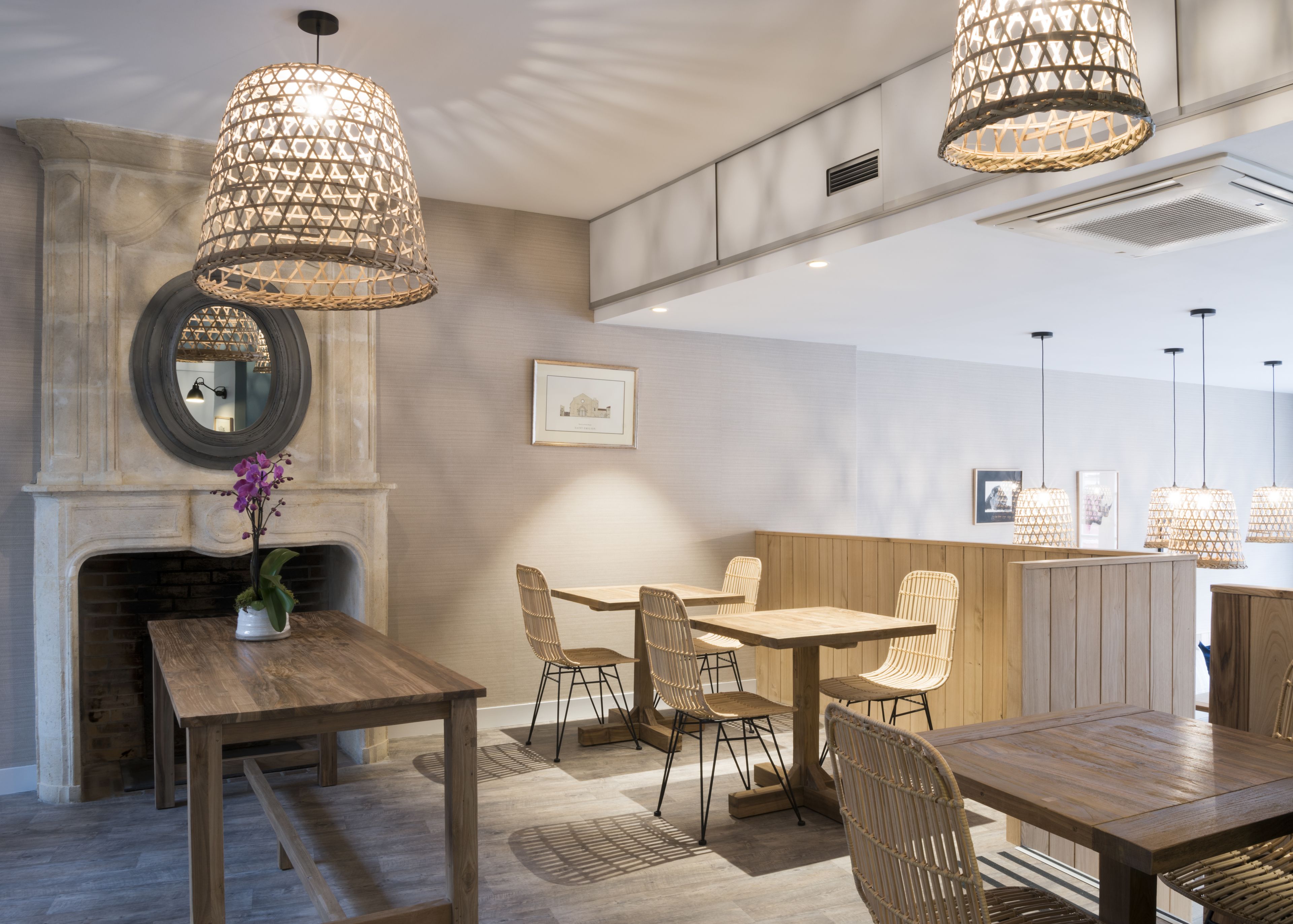 A dining area with wooden tables and chairs, a fireplace, and hanging wicker lamps.