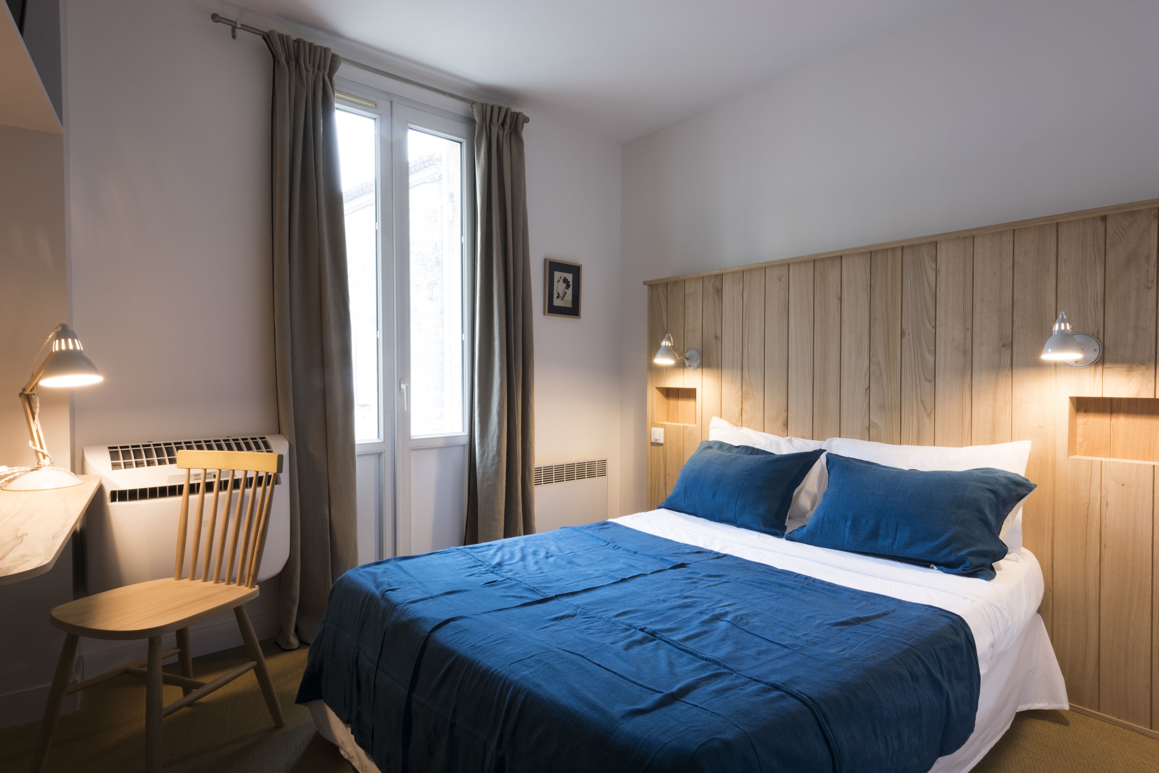 A bedroom with a bed, a desk, a chair, and a window with curtains.