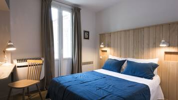 A bedroom with a bed, a desk, a chair, and a window with curtains.