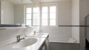 A modern bathroom with two sinks, a bathtub, and a large mirror.