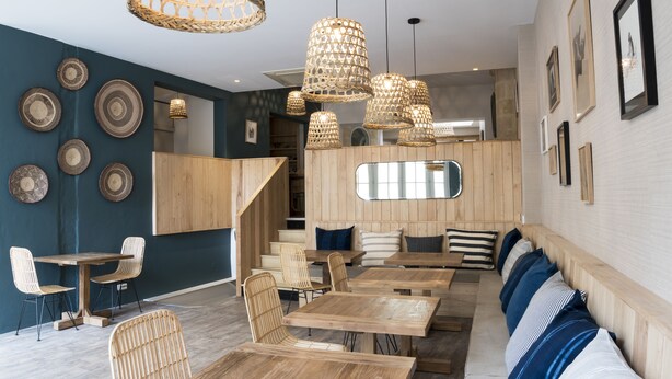 A modern interior with wooden tables and chairs, a staircase, and decorative wall plates. - Auberge de la Commanderie (Saint-Émilion)