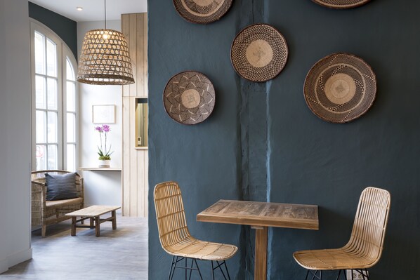A room with a wooden table and two wicker chairs, a hanging light fixture, and three woven wall decorations.