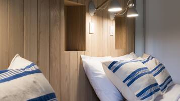 A hotel room with wooden panel walls, two beds with striped bedding, and wall-mounted lamps.