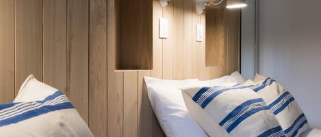 A hotel room with wooden panel walls, two beds with striped bedding, and wall-mounted lamps.