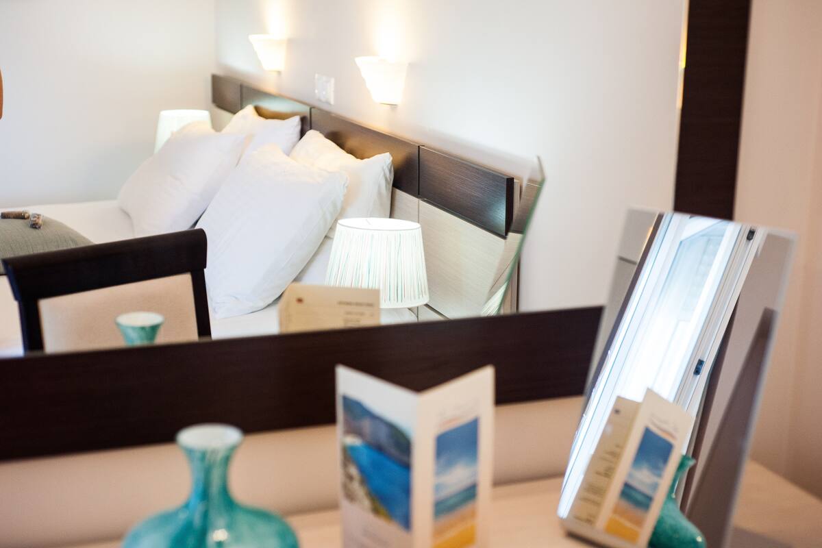 A hotel room with a bed, nightstands, a lamp, and a mirror reflecting the room.