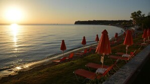 Vista de la playa con agua iluminada por el sol, sombrillas rojas y sillas de descanso.