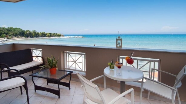 Un balcón con vistas al mar, una mesa con bebidas y asientos.