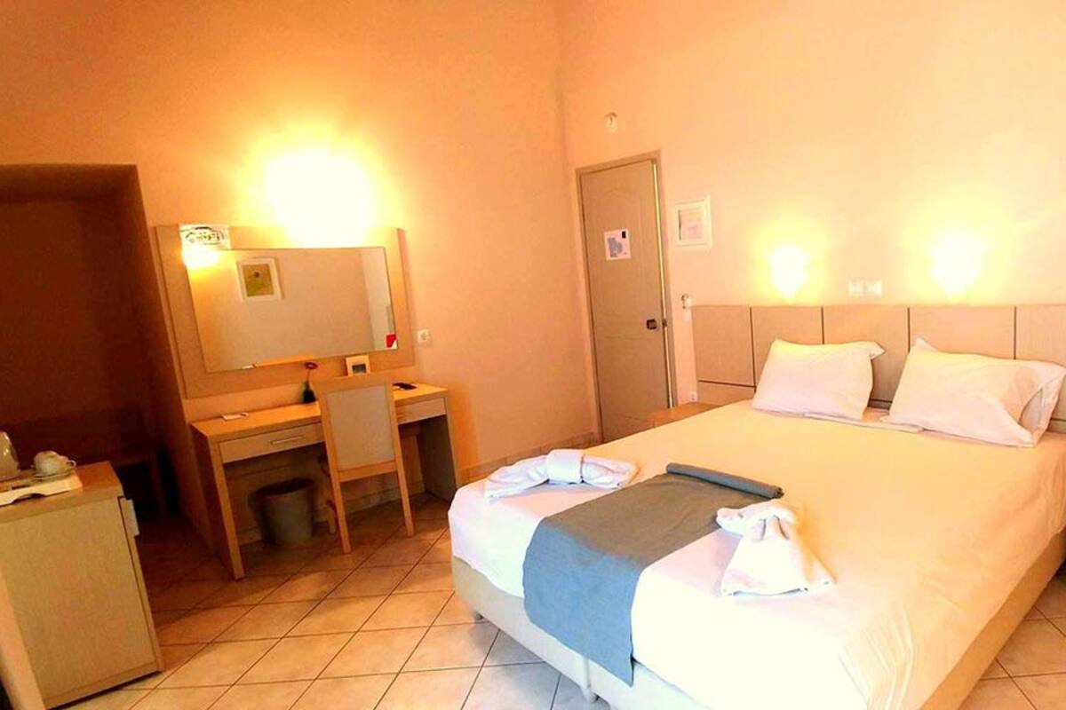 A hotel room with a bed, bedside table, desk, chair, and a small cabinet.