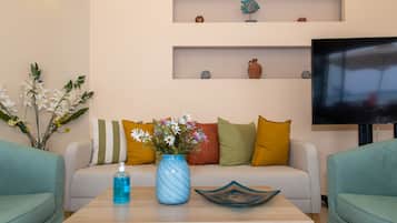 A living room with a sofa, a coffee table, a TV, and decorative items on shelves.