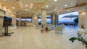 Un vestíbulo amplio con zona de bar, arreglos de asientos y un gran ventanal con vista al mar.